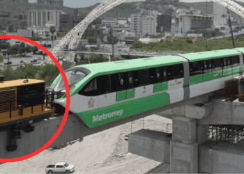 Elevated green-and-white metro train beside a yellow maintenance vehicle at a construction site.