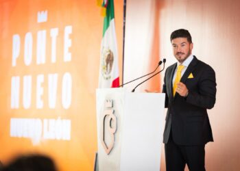 Man in a Dark Suit and Yellow Tie Speaks at a Podium, with a Mexican Flag Behind Him and an Orange Backdrop. › La Sierra Madre