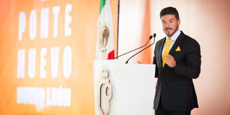 Man in a Dark Suit and Yellow Tie Speaks at a Podium, with a Mexican Flag Behind Him and an Orange Backdrop. › La Sierra Madre